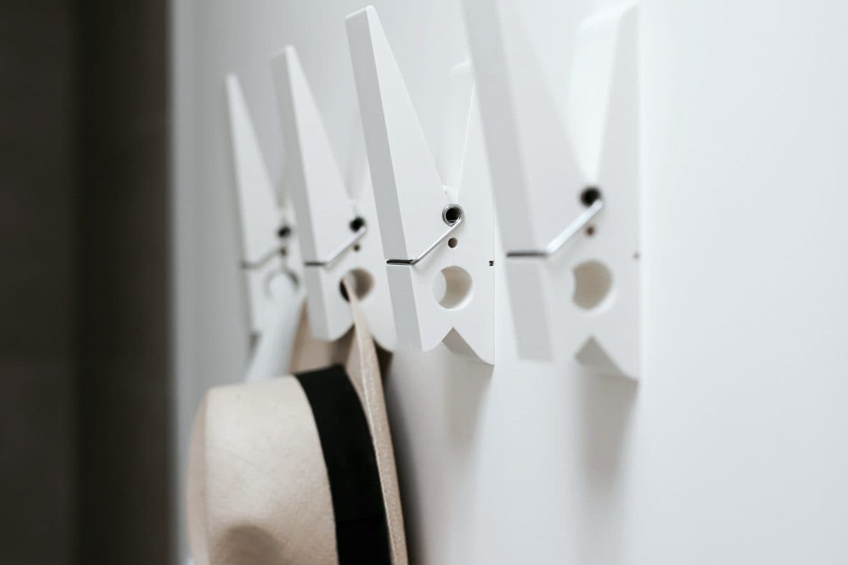 Four white wall hooks on a smooth white wall, with a straw hat on the nearest hook