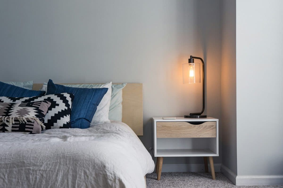 A made bed with white bedding and blue pillows beside a nightstand with a lit lamp