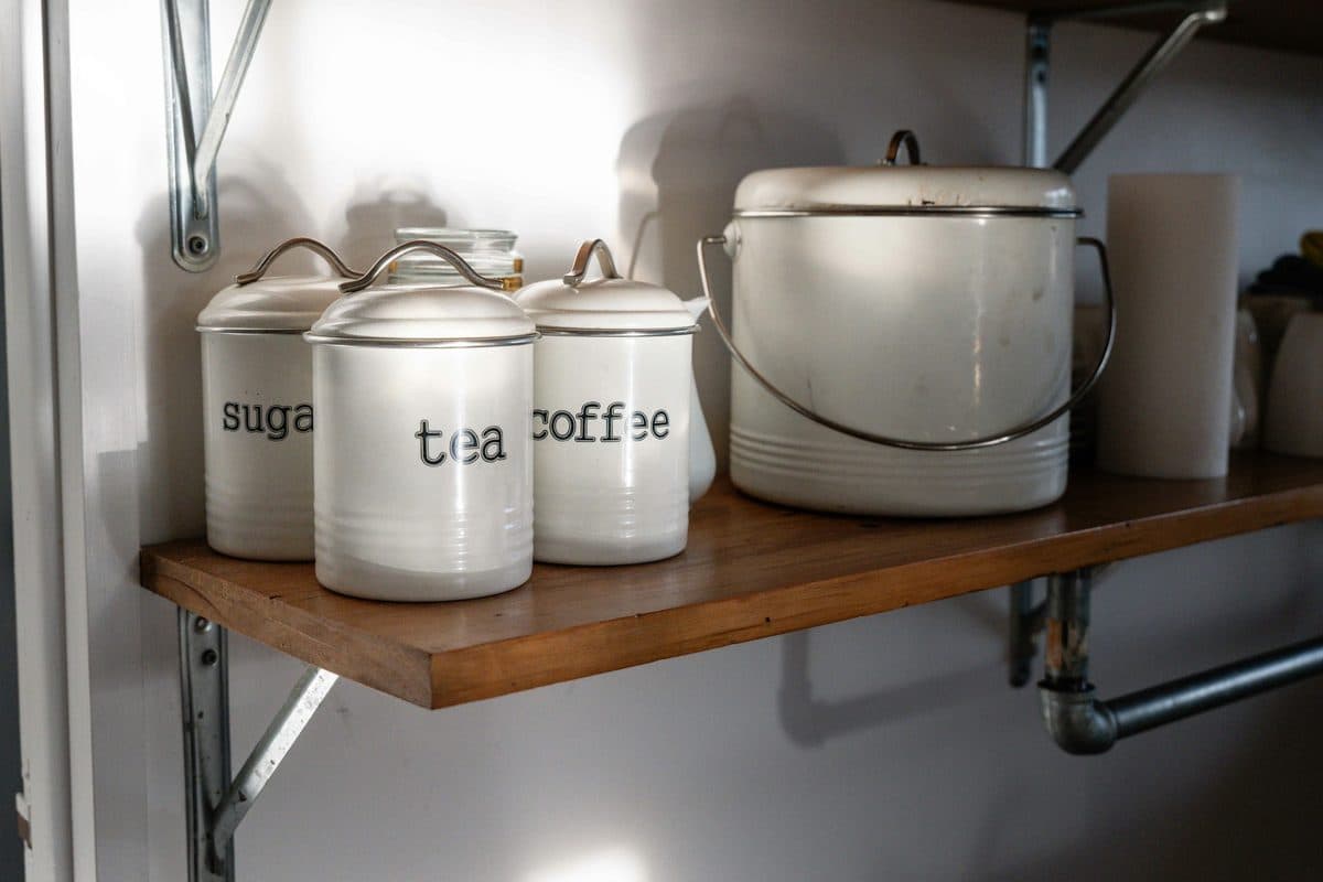 White canisters on a wood pantry shelf, with tea and coffee labels readable and a third canister at the left edge
