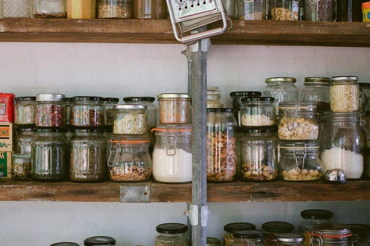 Tiny kitchen pantry shelves organized into labeled zones with clear jars, bins, and a simple restock basket