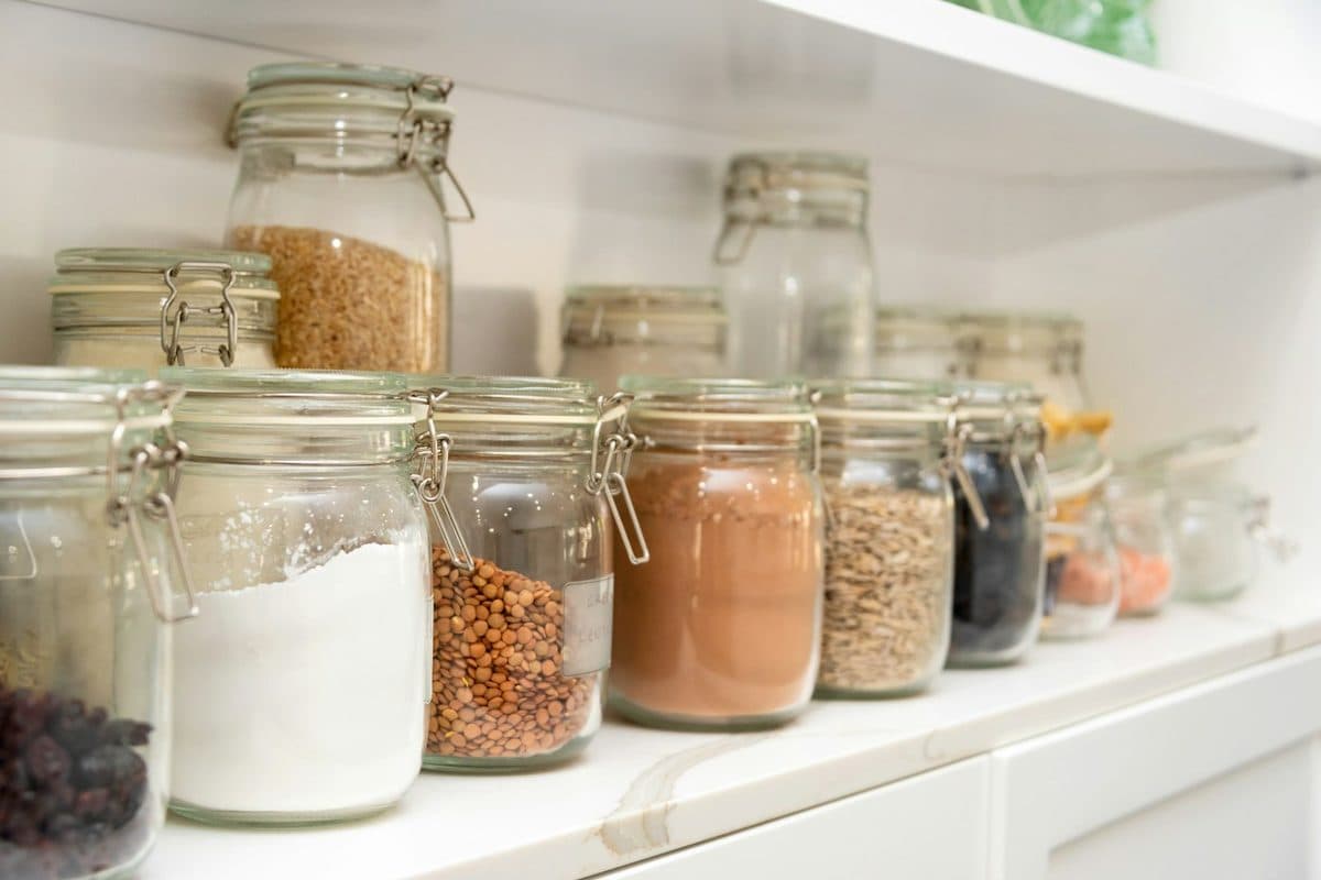 Glass jars of dry goods lined up on a white pantry shelf
