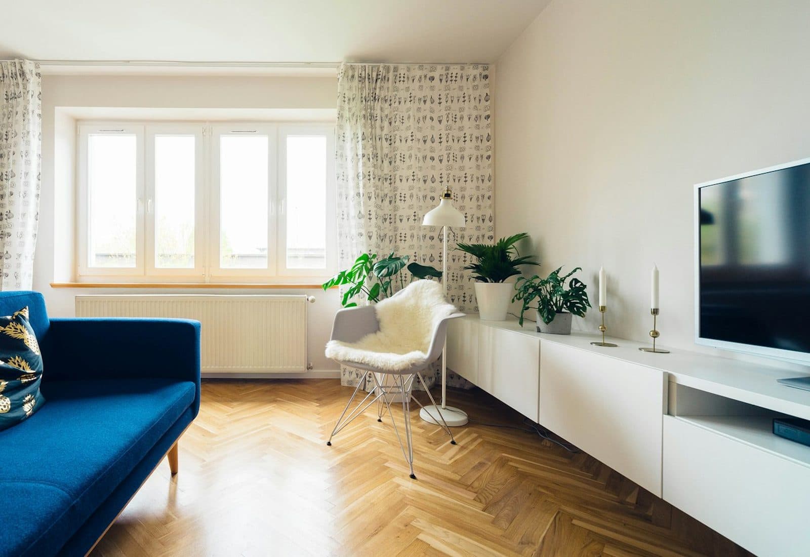 Bright small living room with a blue sofa, plants, a white media console, and a clear wood floor