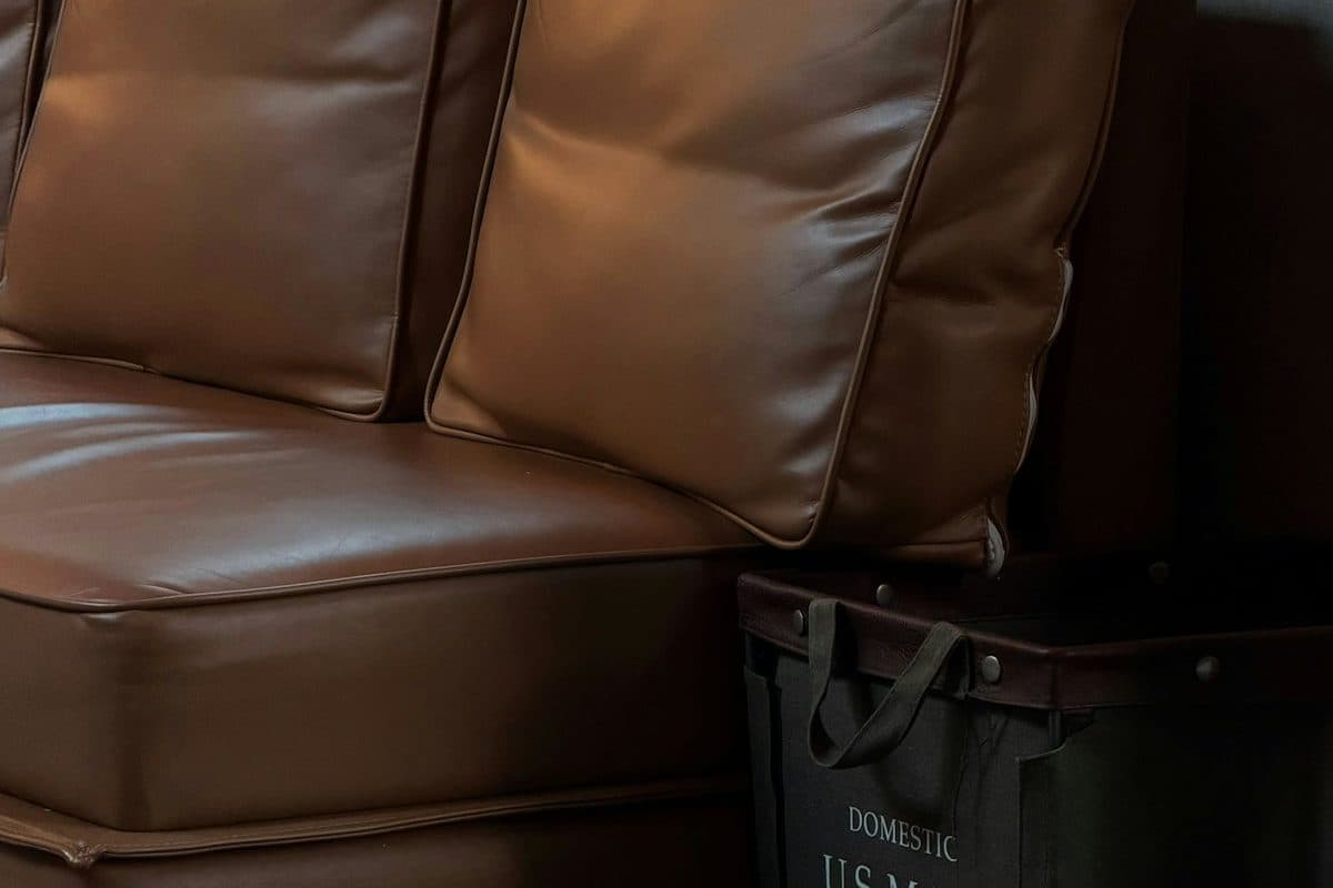 A brown leather sofa with a canvas mail bin on the floor beside the seat