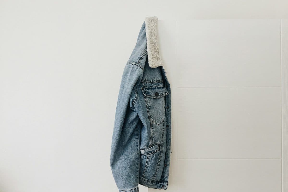 A denim jacket hanging over the top edge of a white door