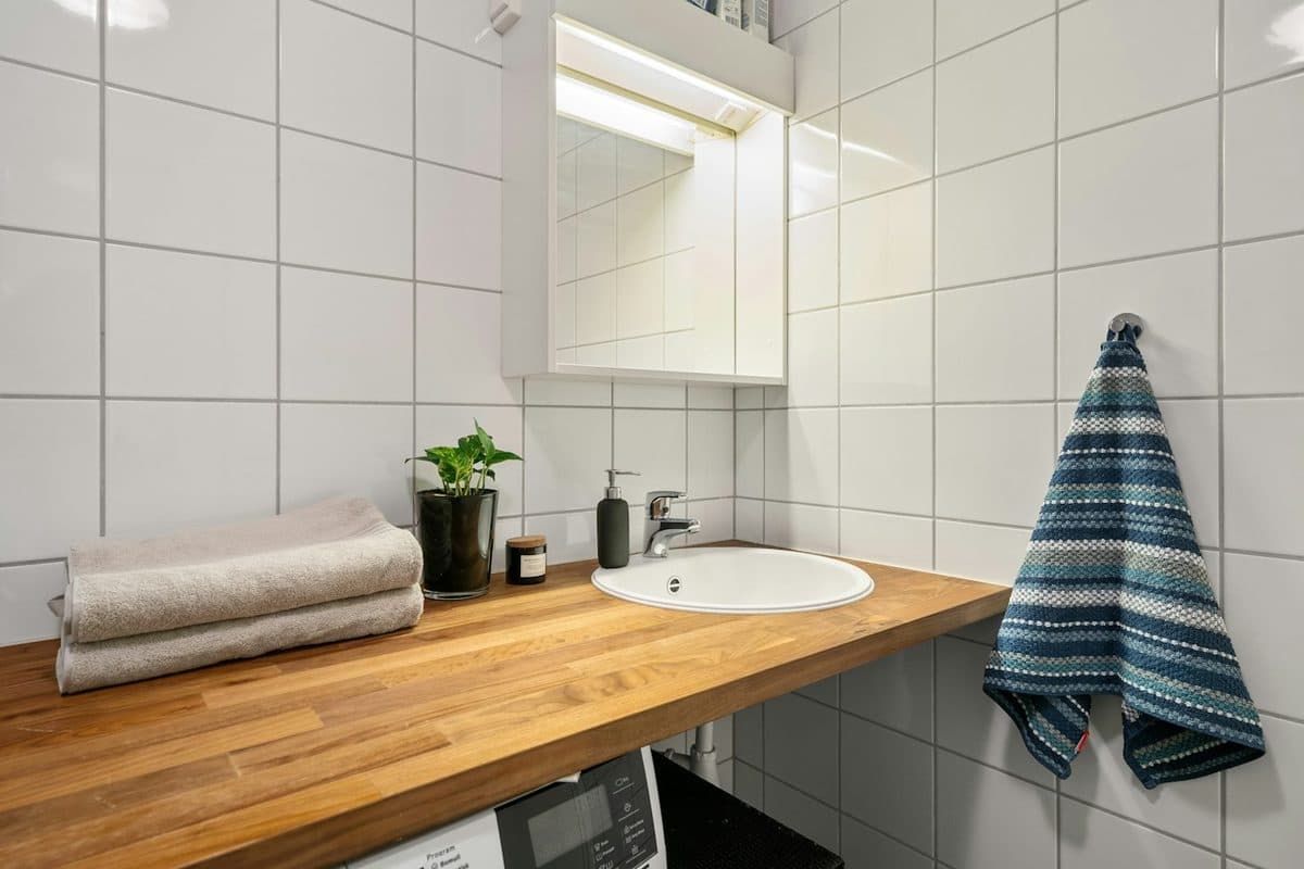 A small bathroom sink with a wood counter, a bar of soap, two folded towels, and a striped towel on a hook