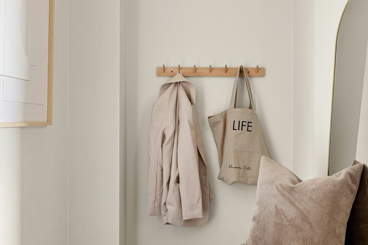 Narrow entry with a wood peg rail holding a coat and a tote, plus a woven bench
