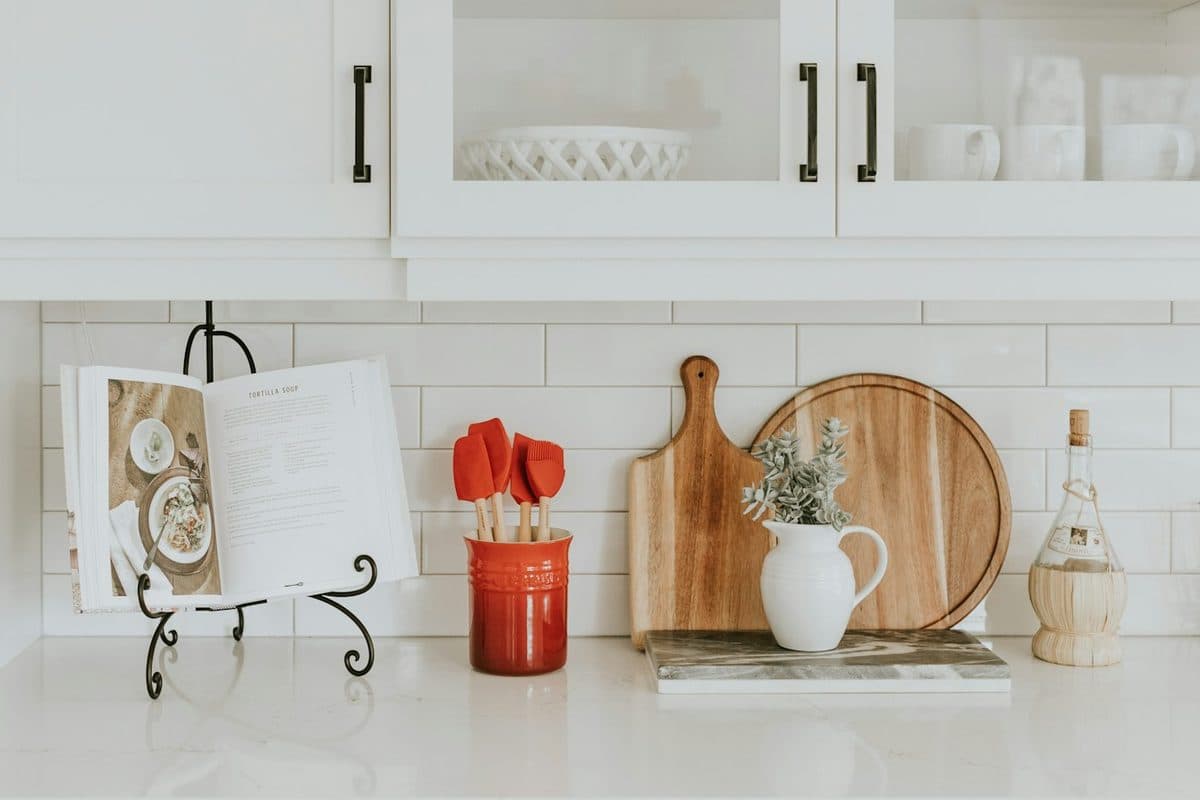 White kitchen counter with a utensil crock, cutting boards, a small pitcher, and a cookbook