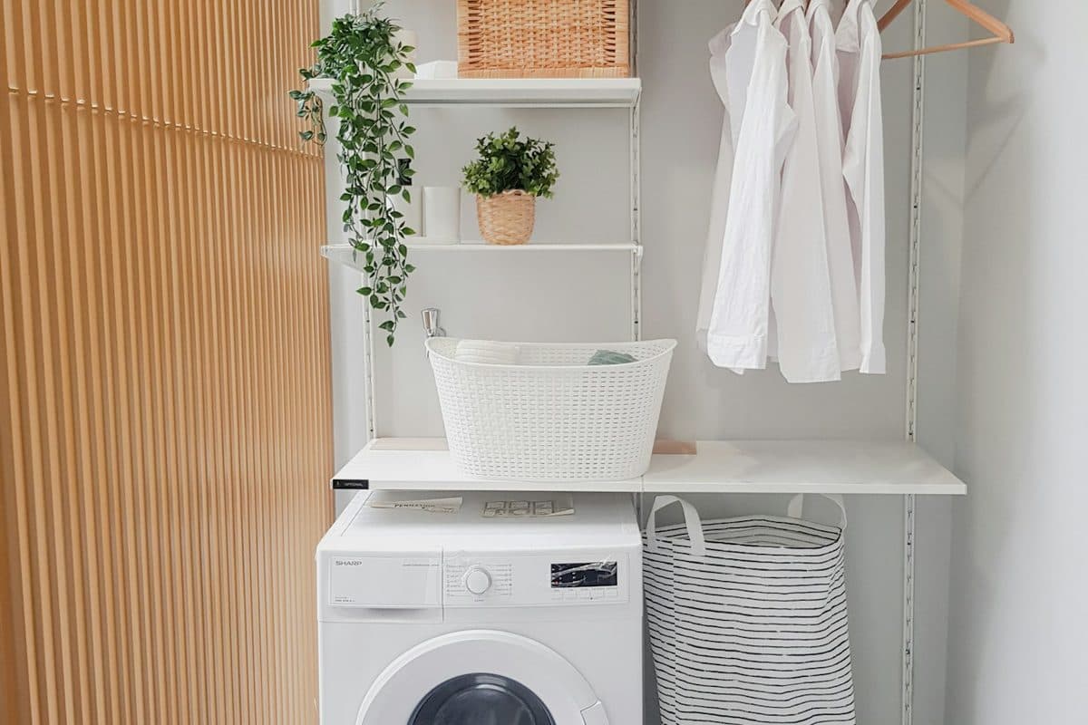 Small laundry nook with a front-load washer, a shelf and hanging rod above it, and a striped hamper beside the machine