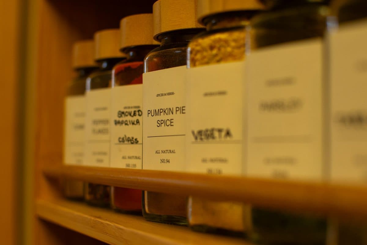 Labeled spice jars in a row on a wooden shelf, including pumpkin pie spice and smoked paprika