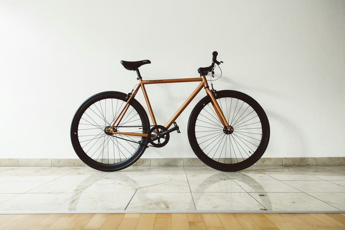 A brown bicycle standing indoors against a plain white wall, both wheels on a tile floor