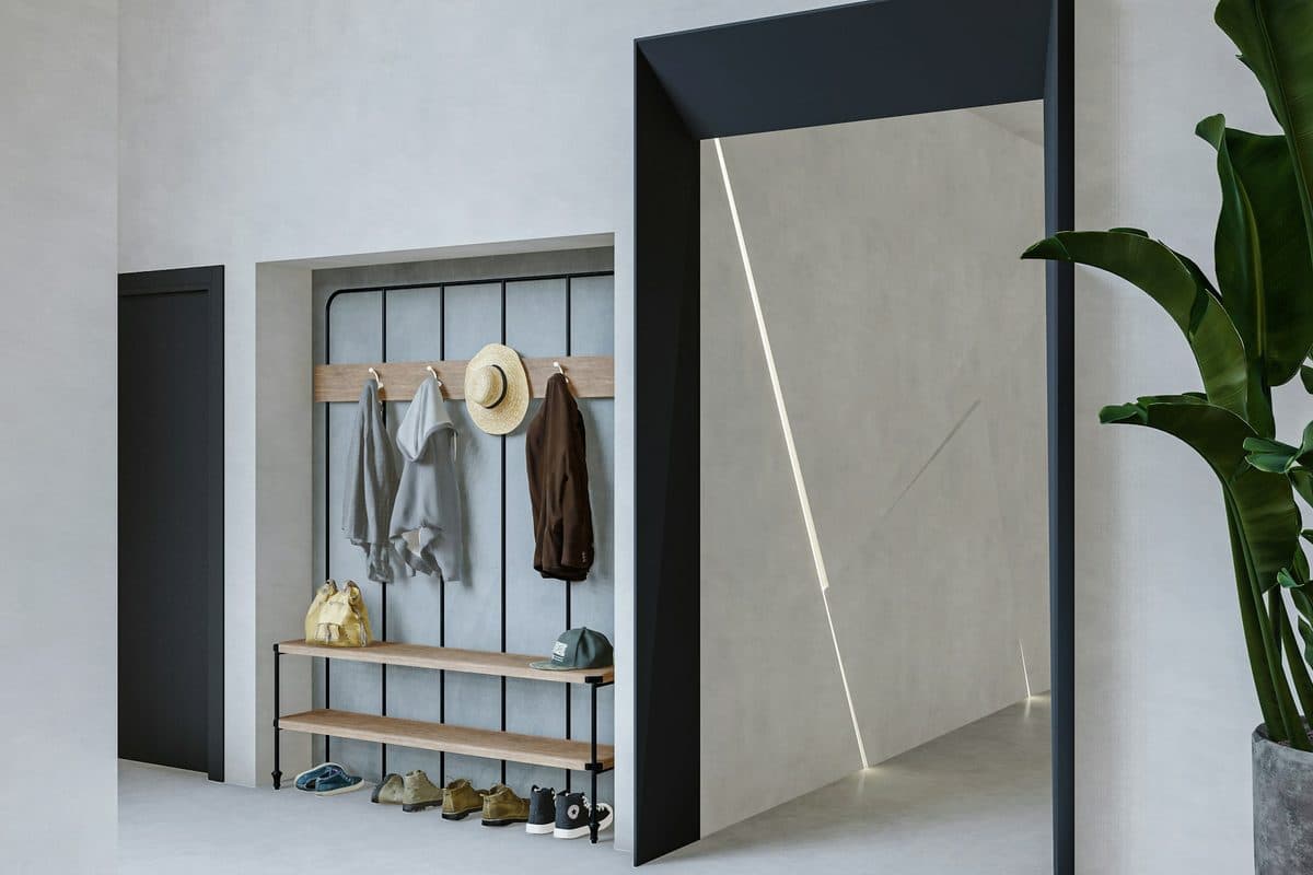A small entry alcove with three jackets and a straw hat on a wood rail, shoes on the shelves below, and a large plant by the doorway